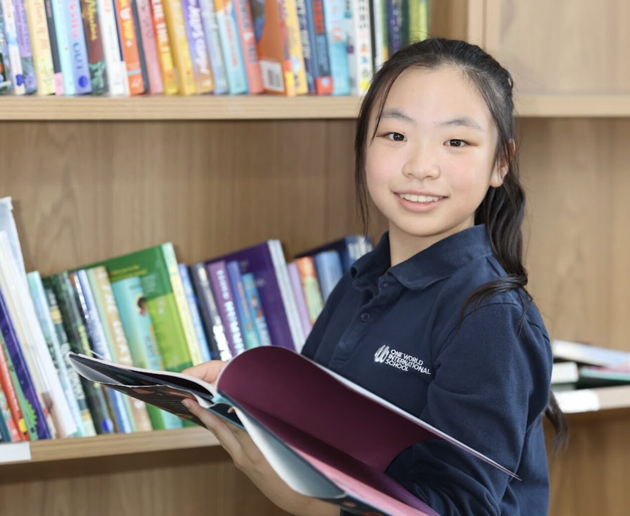 Primary school age Girl student holding book in library at OWIS Osaka