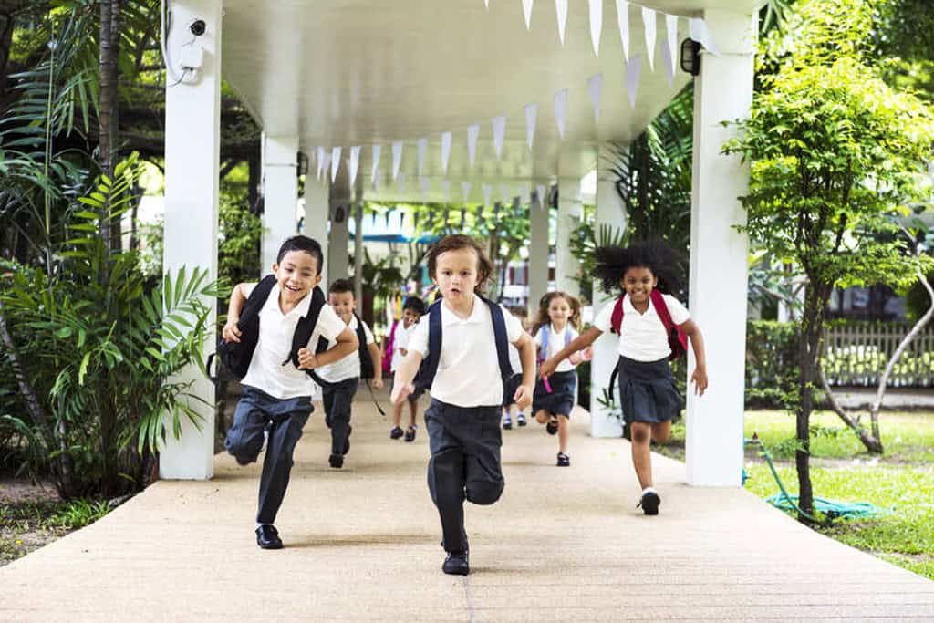 身穿校服的小学生们笑容满面地在操场上奔跑的场景