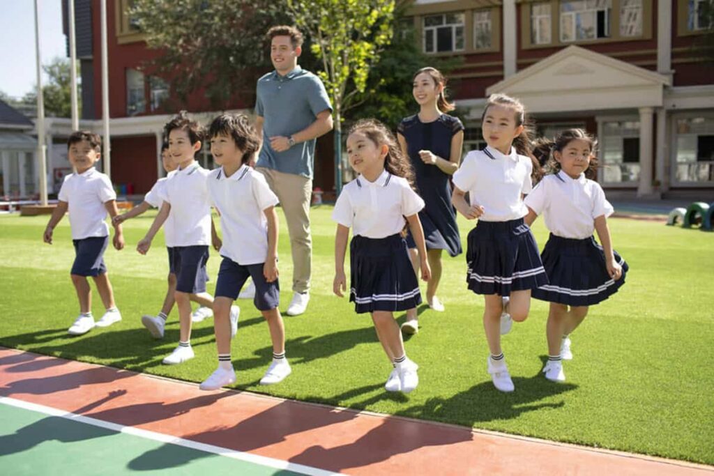 校庭を歩く制服姿の子供たちと先生