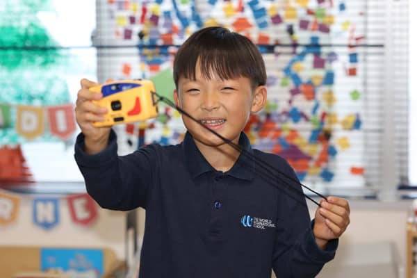 Early Childhood (EC) student, safe, happy, and engaged in learning, playing with a camera in the classroom