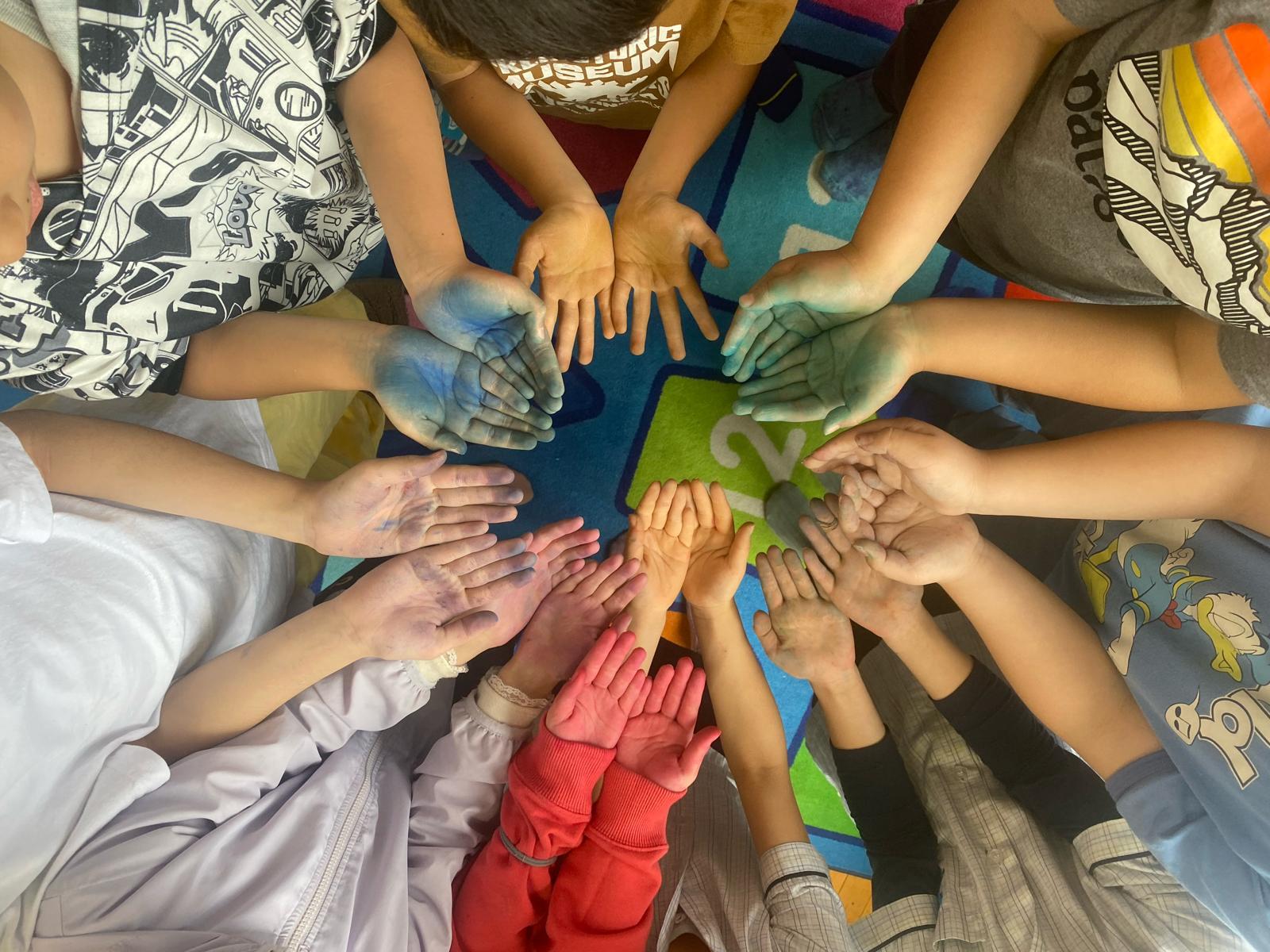 Children at OWIS Osaka taking part in a group activity promoting positive shared values. The kids have their hands together in a circle and are painted different colours Children at OWIS Osaka taking part in a group activity promoting positive shared values. The kids have their hands together in a circle and are painted different colours