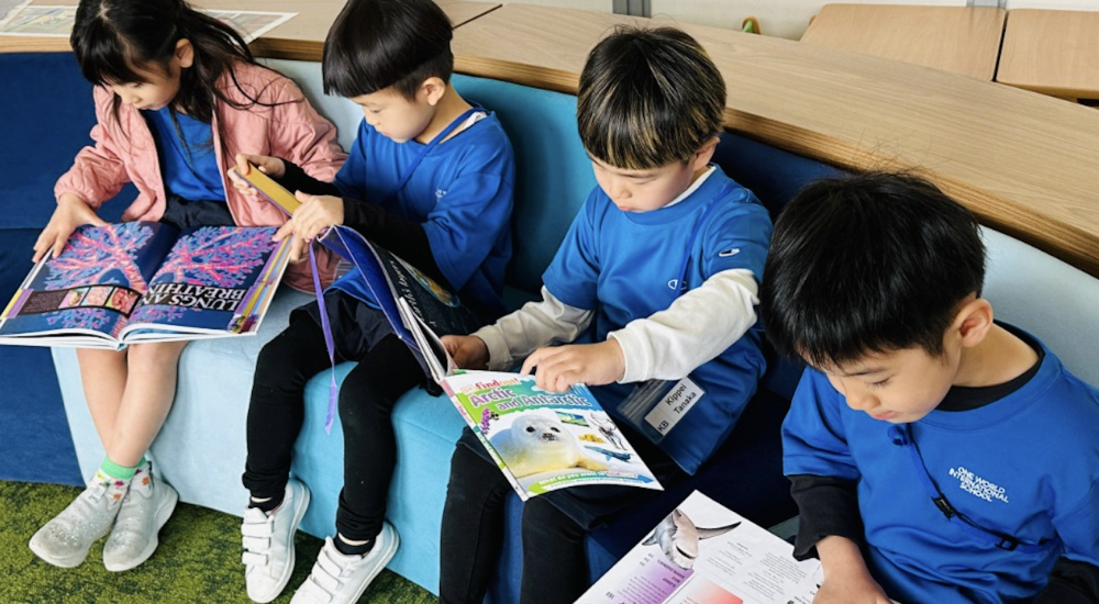 One World international School Osaka Students learning in the library holding books One World international School Osaka Students learning in the library holding books
